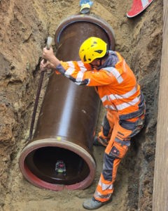 Bauarbeiter installiert großes Abwasserrohr im Graben