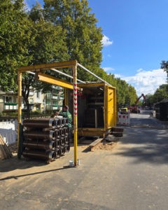 Baustelle mit Rohren und gelbem Container auf Straße