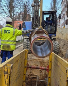 Bauarbeiter verlegen großes Rohr in Baustellengraben